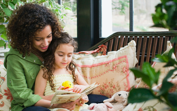Mom and daughter reading on couch in front of window