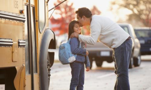 Father kissing daughter near school bus