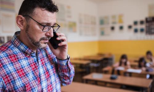 Man talking on a phone with students in the background