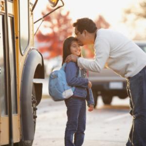 Father kissing daughter near school bus