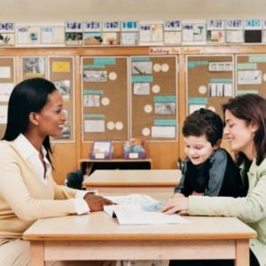 A teacher talking with a woman and boy at a classroom table.