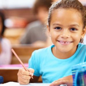 A girl smiling into the camera with a pencil in her hand.