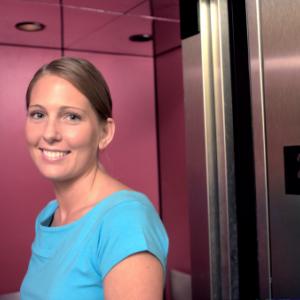 Woman standing in front of an elevator and smiling at the camera.