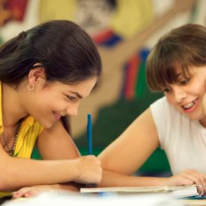 Two smiling young adults looking at what one of them is writing.