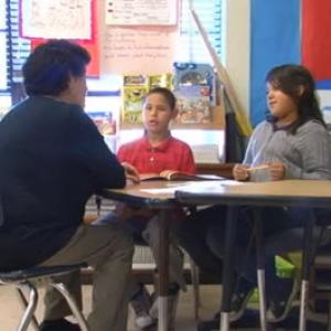 A man sitting at a classroom table with two students.