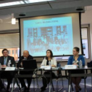 Six adults sitting at tables in front of a projector screen.