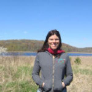 a woman standing in front of a lake and smiling at the camera