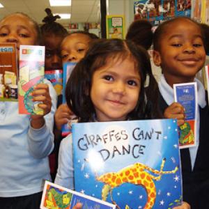 Smiling children holding up books in front of them.