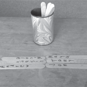 A black and white photo of a cup of popsicle sticks on a table and six are laid out.