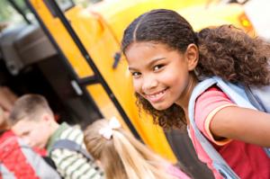 girl smiling at the camera as she gets on a school bus