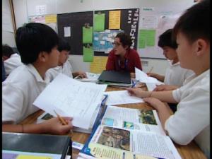 four students and a teacher sit at a table with papers and books in front of them