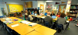 a wide shot of a classroom with adults sitting around a table