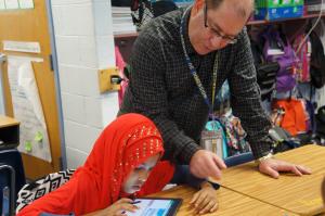 a man helping a young girl in a hijab with a tablet computer