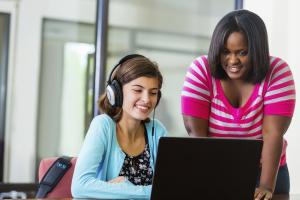 two young women looking at a laptop screen and one has on headphones