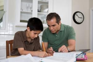 a man and a boy sitting at the kitchen table working on homework