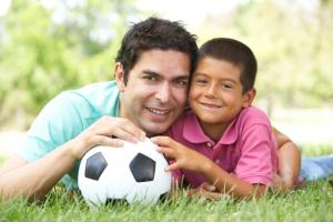 boy and man laying in the grass holding a soccer ball