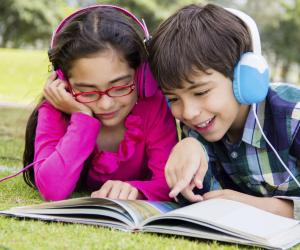 two children in headphones looking at a book.