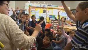 a group of children in a classroom all raising their hands