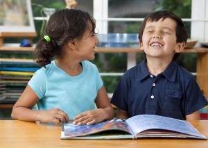 two kids laughing with a book on the table in front of them