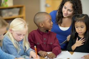 three kids and an adult sitting at a table and one kid is writing