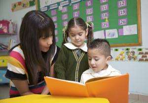 a woman looking at a book with two children. the boy is reading.