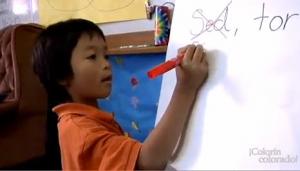 A young boy is writing on a large pad of paper that's on an easel