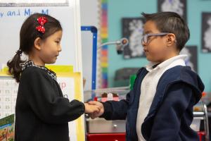 Boy and girl shaking hands in kindergarten classroom