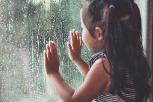 A young girl looking out a window at the rain.