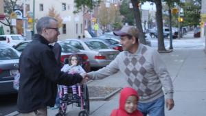 Two men shaking hands in the street with a girl in a wheelchair behind them.
