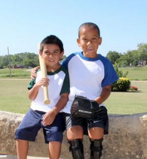 Two boys in baseball uniforms smiling at the camera.