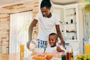Father talking on cell phone while giving son breakfast