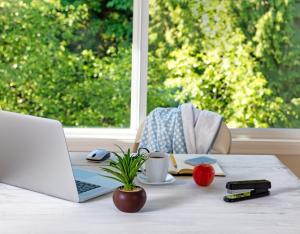 A desk with a laptop, plant, coffee, stapler, mouse, pencil, apple, and notebook.