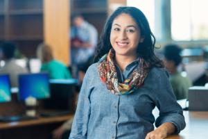 A teenager standing in the library and smiling at the camera.