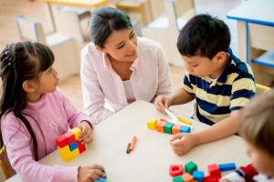 A woman smiling at two kids who are playing with blocks.