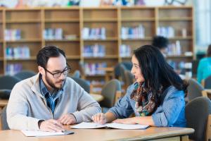 A man looking at workbooks with a teenage girl in the library.