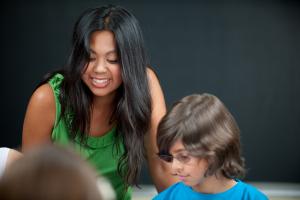 A woman smiling as she helps a chlid with his work