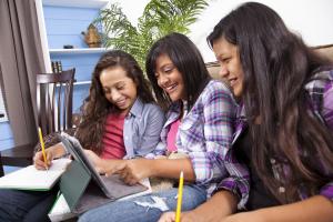 Three girls smiling as they do work on a tablet computer