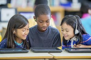 three children looking at a tablet while wearing headphones