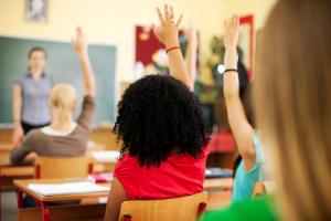 A shot from behind of children raising their hands in class