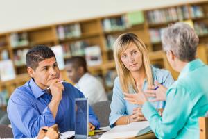 Three adults sitting at a table and talking in the library