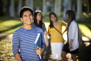 a young man holding a book at smiling at the camera