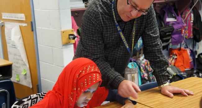 a man helping a young girl in a hijab with a tablet computer
