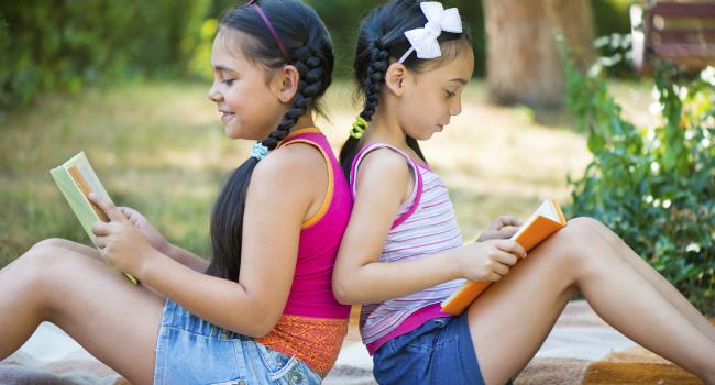 Two young girls sitting back-to-back and reading