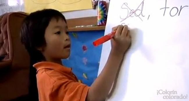 A young boy is writing on a large pad of paper that's on an easel