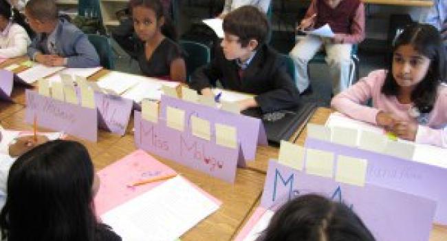 Students at their desks with signs, papers, and sticky notes in front of them.